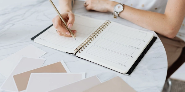 A wedding professional writing in a planner surrounded by color swatches on a marble table