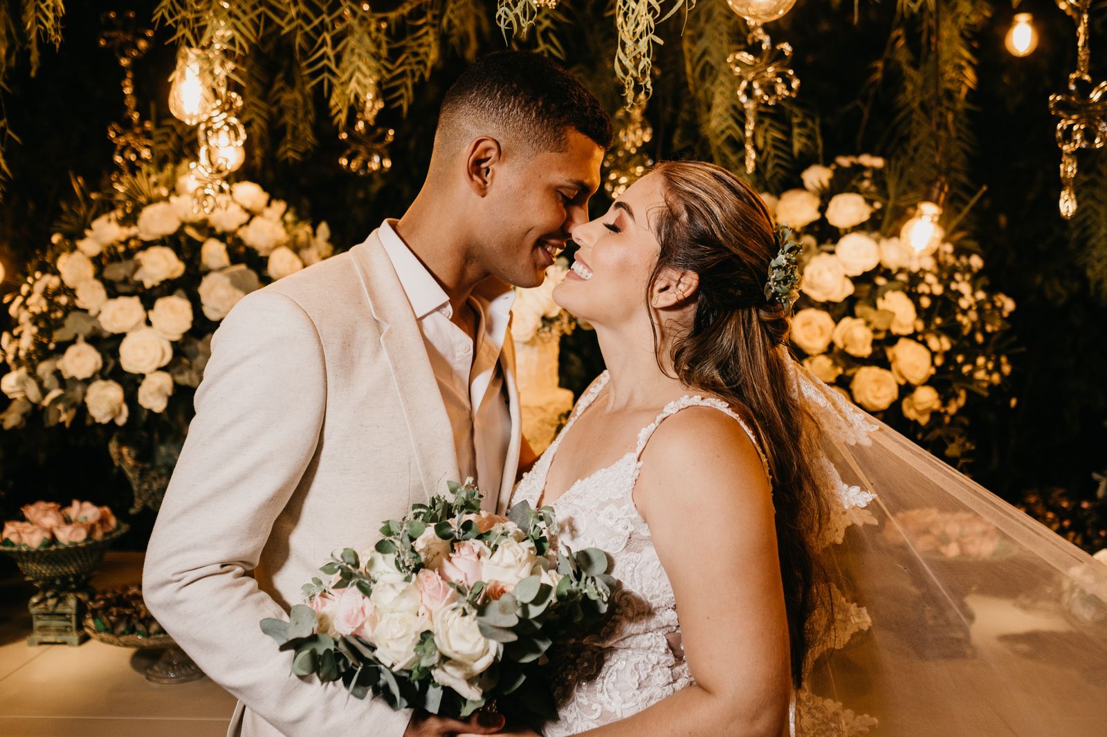 A newly married couple embracing surrounded by warm string lights and roses